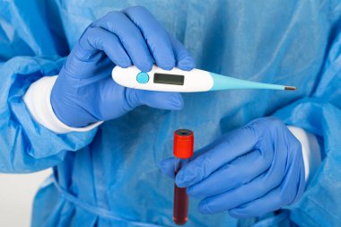 Tıbbi cerrah dijital termometre ve kan örneği tutuyor. COVID-19 test sonuçları