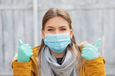 Coronavirus salgını alarmı yüzünden ameliyat maskesi ve eldiven takan genç bir kadının portresi.