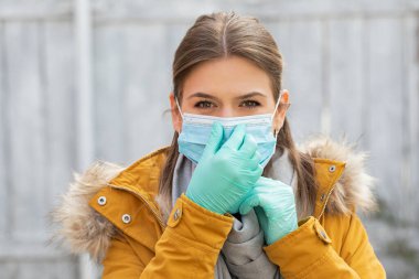 Coronavirus salgını alarmı yüzünden ameliyat maskesi ve eldiven takan genç bir kadının portresi.