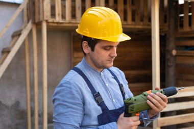 Elinde elektrikli matkap tutan sarı kasklı yakışıklı bir zanaatkarın portresi. 