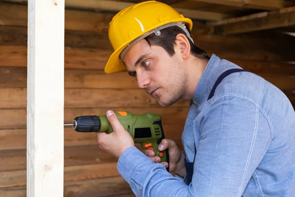 Portrait of a handsome young craftsman with yellow hard hat holding an electric drill