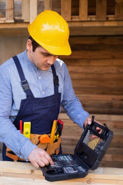Sarı şapkalı ve üniformalı tamirci dışarıda yenileme projesi için araç tutuyor.