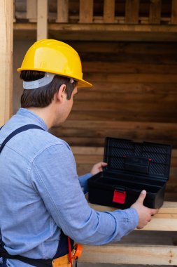 Sarı kasketli, mavi gömlekli, ahşap arka planda genç bir marangoz.