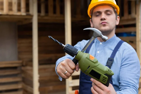 Handsome young repairman holding construction tools in front of wooden background