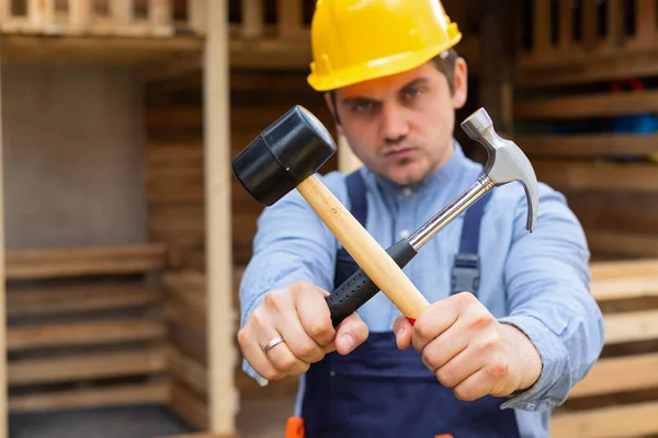 Handsome young repairman holding construction tools in front of wooden background