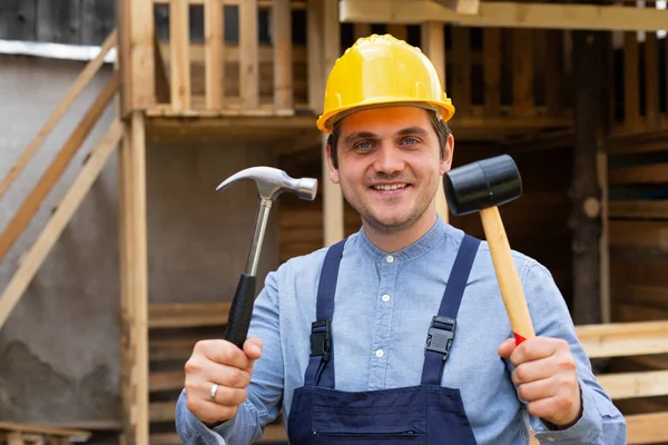 Handsome young repairman holding construction tools in front of wooden background