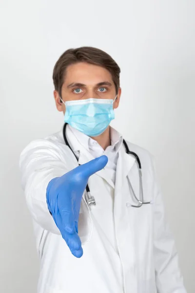 外科マスクを身に着けているハンサムな若い医師は白い背景に握手を示しています — ストック写真
