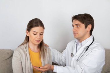 Genç erkek doktor, evde grip belirtileri gösteren kadın hastaya danışıyor.