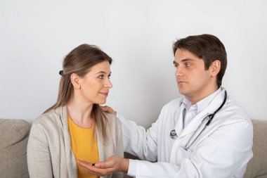 Genç erkek doktor, evde grip belirtileri gösteren kadın hastaya danışıyor.