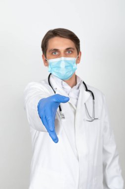 Cerrahi maske takan yakışıklı genç doktor beyaz arka planda el sıkışma gösteriyor.