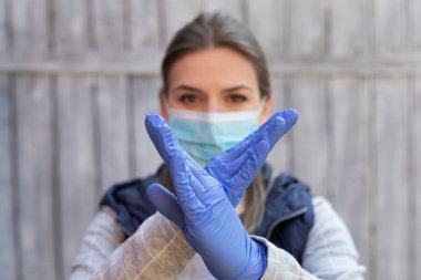 Young caucasian woman with surgical mask and gloves showing an X sign with hands outdoo clipart