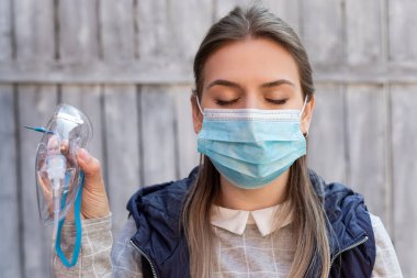 Cerrahi maske takan kadın dışarıda tıbbi oksijen maskesi tutuyor. Koronavirüs salgını.