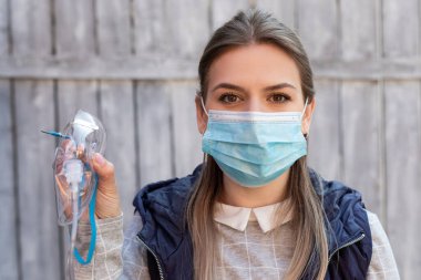 Cerrahi maske takan kadın dışarıda tıbbi oksijen maskesi tutuyor. Koronavirüs salgını.
