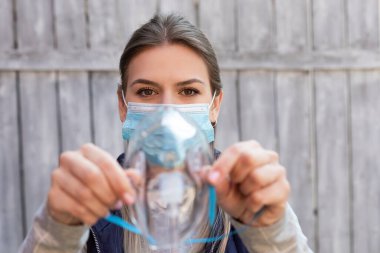 Cerrahi maske takan kadın dışarıda tıbbi oksijen maskesi tutuyor. Koronavirüs salgını.