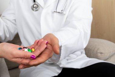 Doktorun kadın hastaya ilaç ve takviye verirken yakın plan fotoğrafı, ikisi de koltukta.