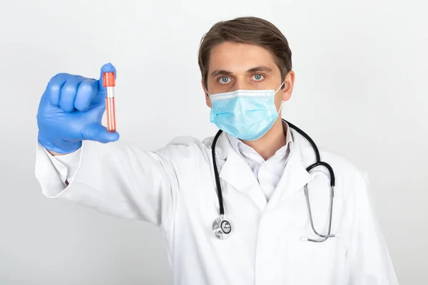 若いです男性医師とともに外科用マスクと手袋ホワイトの背景に血液サンプルを保持 — ストック写真