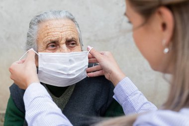 Hemşire yaşlı hasta kadına cerrahi maske takıyor. Koronavirüs koruma protokolü.