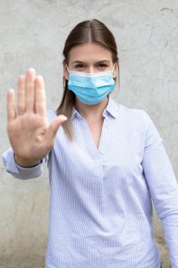 Cerrahi maske takan genç beyaz kadın elleriyle dur işareti gösteriyor- koronavirüs karantinası