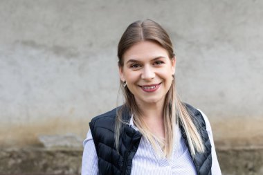 Dışarıdaki kameraya gülümseyen beyaz bir kadının portresi.