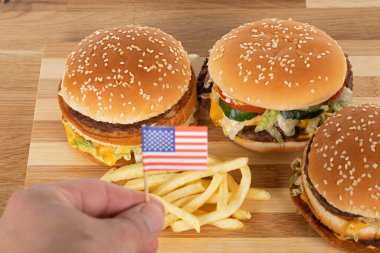 Tahta masada leziz hamburgerler ve patates kızartmaları ve Amerikan bayrağını tutan insan eli.