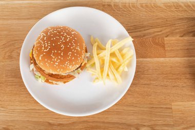 Sebzeli lezzetli çizburger ve susamlı çörek ve ahşap masada patates kızartması.