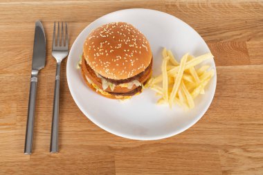 Sebzeli lezzetli çizburger ve susamlı çörek ve ahşap masada patates kızartması.
