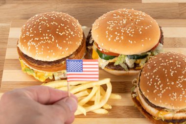 Tahta masada leziz hamburgerler ve patates kızartmaları ve Amerikan bayrağını tutan insan eli.