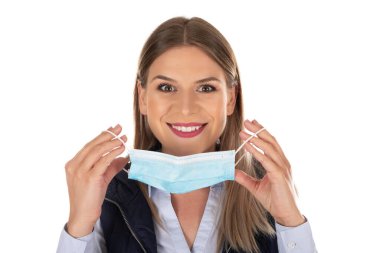 Cerrahi maskeli beyaz kadın portresi izole edilmiş arka planda kameraya gülümsüyor.