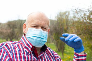 Dışarıdaki tekerlekli sandalyede oturan cerrahi maskeli yaşlı bir adam - enfeksiyon kapma riski