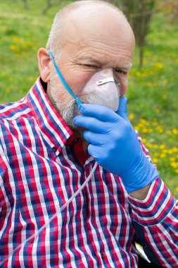 Oksijen maskeli yaşlı bir adamın portresi bahçede vakit geçiriyor. Koronavirüs karantinası.