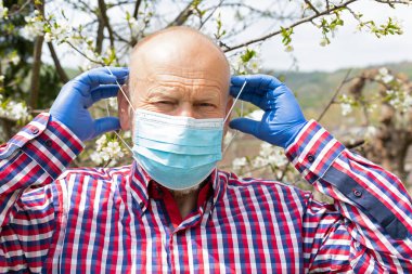 Cerrahi maskeli yaşlı bir adamın portresi bahçede vakit geçiriyor. 