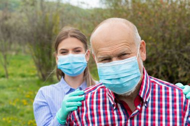 Tekerlekli sandalyede oturan engelli yaşlı bir adam, dışarıda genç bir bayan bakıcı var.