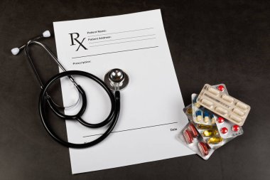 Hastanın bilgi kaydı, steteskop ve koyu arkaplandaki ilaçların fotoğrafı.