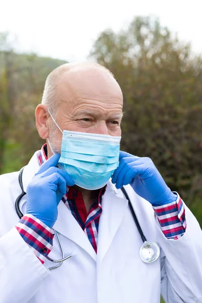 Dışarıda Poz Veren Üniformalı Cerrahi Maskeli Kıdemli Erkek Doktorun Portresi — Stok fotoğraf