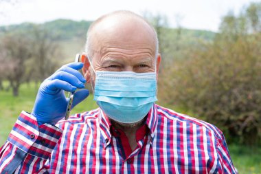 Cerrahi maske takan ve dışarıda telefonla konuşan yaşlı bir adamın portresi.