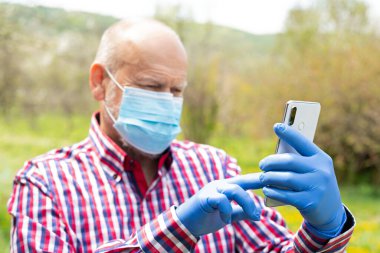 Cerrahi maske takan ve dışarıda telefonla konuşan yaşlı bir adamın portresi.