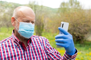 Cerrahi maske takan ve dışarıda telefonla konuşan yaşlı bir adamın portresi.