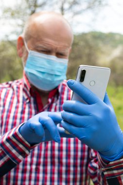 Cerrahi maske takan ve dışarıda telefonla konuşan yaşlı bir adamın portresi.