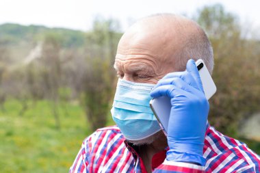 Cerrahi maske takan ve dışarıda telefonla konuşan yaşlı bir adamın portresi.