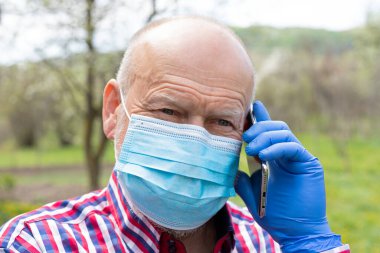 Cerrahi maske takan ve dışarıda telefonla konuşan yaşlı bir adamın portresi.
