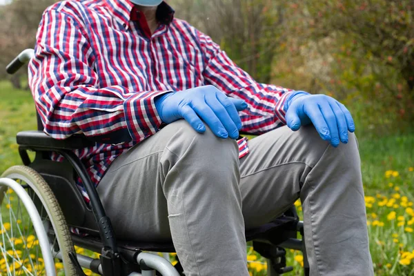 Close up picture of disabled elderly man\'s hand wearing gloves in time of covid-19 pandemic, sitting in a wheel chair outdoors