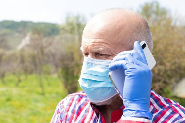 Cerrahi maske takan ve dışarıda telefonla konuşan yaşlı bir adamın portresi.