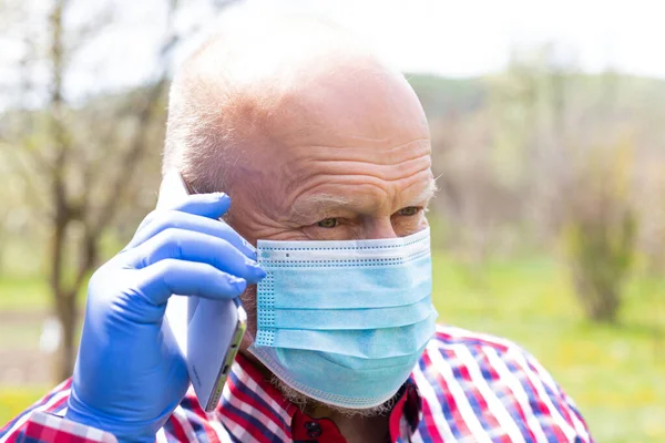 Cerrahi maske takan ve dışarıda telefonla konuşan yaşlı bir adamın portresi.