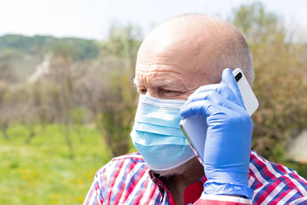 Cerrahi maske takan ve dışarıda telefonla konuşan yaşlı bir adamın portresi.