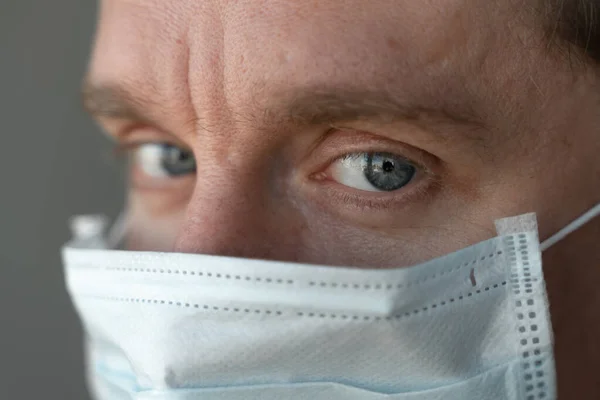 man in medical mask at daytime looking at camera, a very close up shoot of the eyes