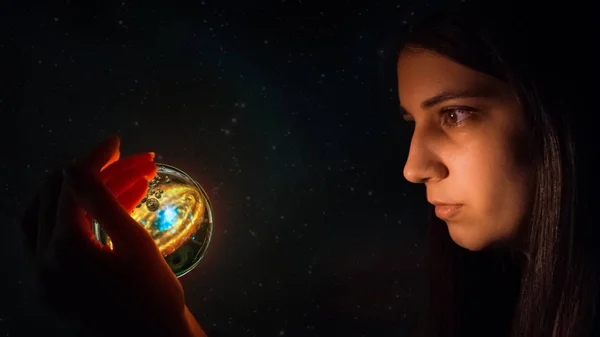 Fortune teller predicts future fate. The Gypsy holds a magic ball in her hand and wonders. Christmas divination. Esoteric and spiritualistic seance. The girl's face lights up the magic ball of fate. — Stock Photo, Image