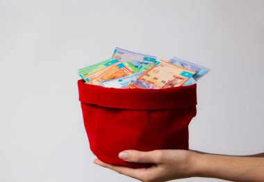 Eller içinde bir sürü tenge olan kırmızı bir çanta tutar. Kazakistan, Kz, Kzt. Ulusal para birimi, banknot. Çok para. İş, ekonomi ve yatırımlar. Zenginlik, birikim, gelir.