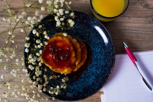 Hermoso desayuno. Panqueques con mermelada y zumo de naranja. Flores y platos elegantes. Un diario con páginas en blanco. Un estilo de vida saludable. Acostado. Decoración de lujo . — Foto de Stock