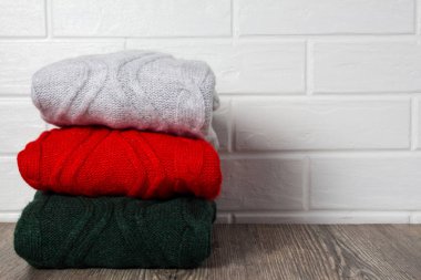 Kıyafet, moda, tarz. Bir yığın renkli kazak beyaz tuğla bir duvarın yanındaki ahşap bir masaya konur. Hygge, rahat, kaşmir, yumuşak. Ev rutini, düzen, depolama.