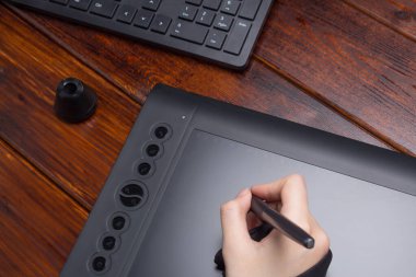 Grafik tasarımcısı dijital tablet üzerinde çalışıyor. El bir grafik tabletine çiziyor. Serbest çalışan, tasarımcı, çizer. Teknoloji, uzaktan kumanda, dış kaynak kullanımı. Grafik tableti için eldiven ve kalem. Proje